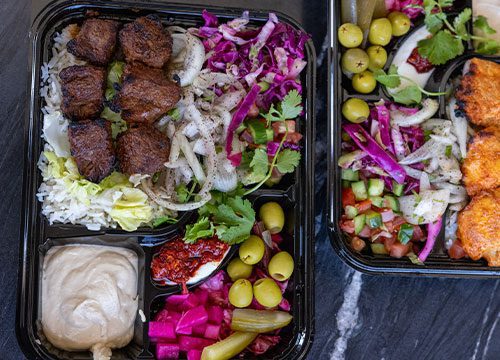 Three black plastic containers with food in them.