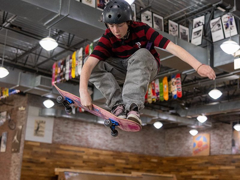 A skateboarder wearing a helmet performs an aerial trick in an indoor skate park.